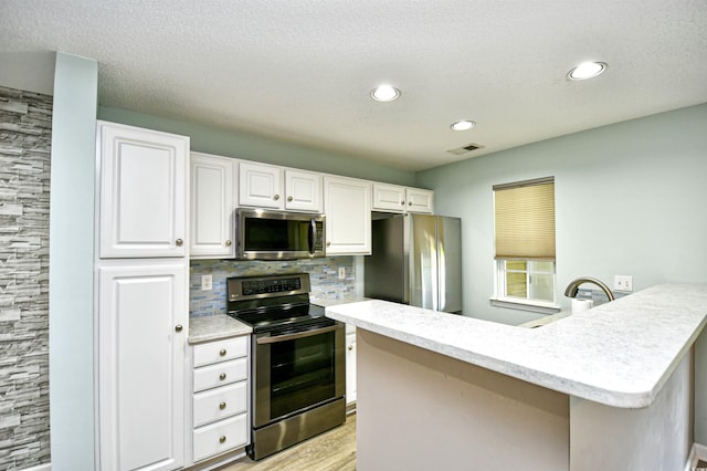 kitchen featuring stainless steel appliances, white cabinets, a peninsula, light wood finished floors, and decorative backsplash
