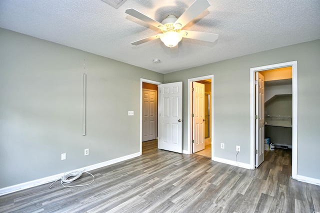 unfurnished bedroom featuring wood finished floors, a walk in closet, baseboards, a textured ceiling, and a closet