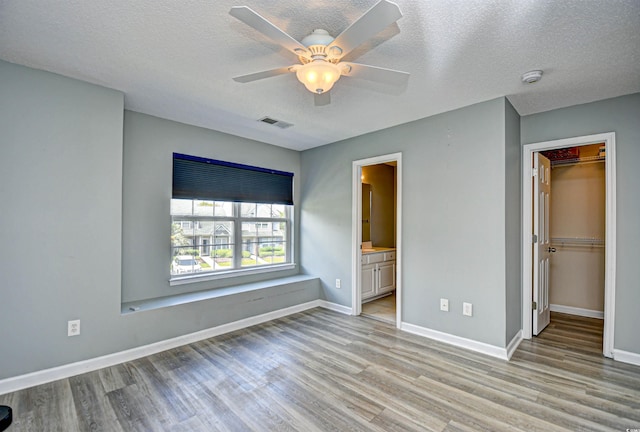 unfurnished bedroom with light wood-style floors, a spacious closet, baseboards, a closet, and a textured ceiling