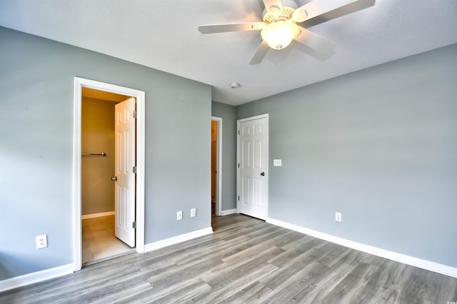 unfurnished bedroom with wood finished floors, baseboards, ceiling fan, and ensuite bathroom