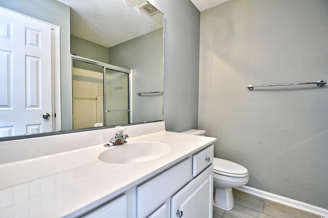 bathroom featuring a stall shower, vanity, a textured ceiling, toilet, and baseboards