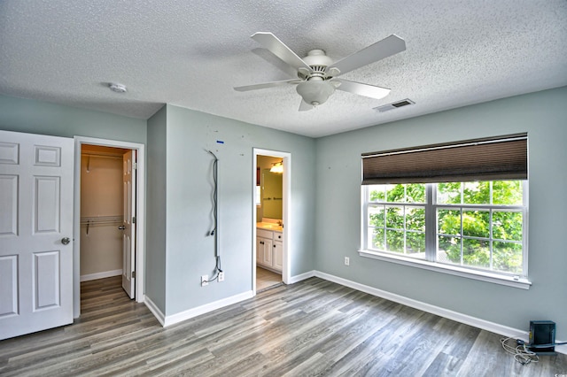 unfurnished bedroom featuring wood finished floors, baseboards, a walk in closet, a textured ceiling, and ceiling fan