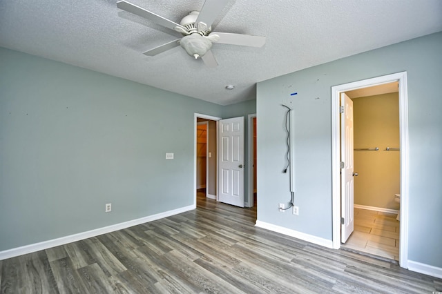 unfurnished bedroom with wood finished floors, a textured ceiling, baseboards, ensuite bathroom, and a ceiling fan