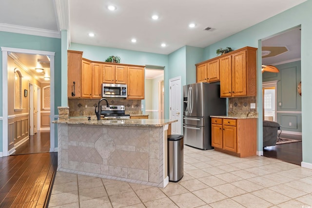 kitchen featuring light stone counters, crown molding, stainless steel appliances, and kitchen peninsula