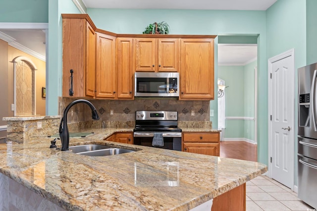 kitchen with tasteful backsplash, ornamental molding, light stone countertops, appliances with stainless steel finishes, and a sink