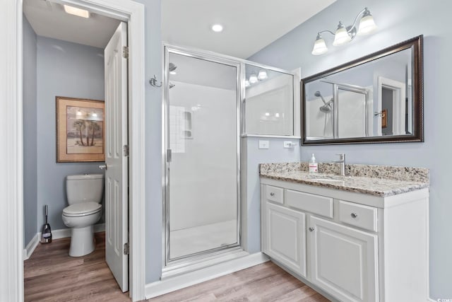 bathroom with toilet, vanity, a stall shower, and wood finished floors
