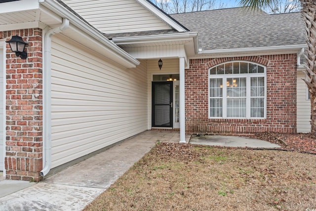 view of exterior entry featuring brick siding and roof with shingles