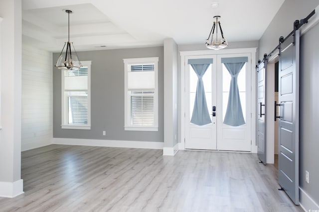 foyer entrance featuring a barn door, baseboards, light wood-style flooring, a tray ceiling, and a chandelier