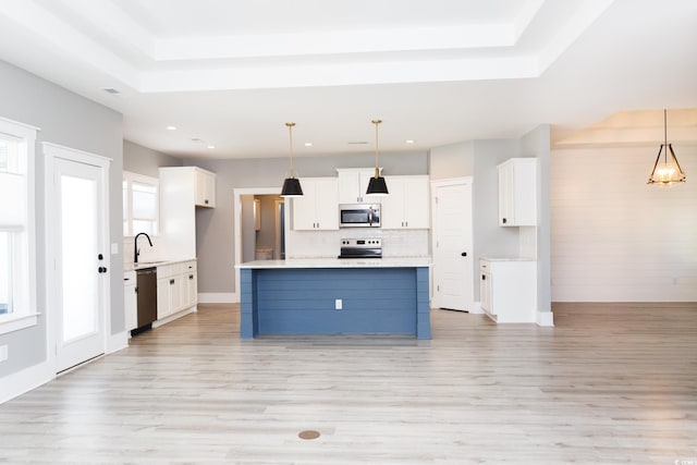 kitchen with stainless steel appliances, white cabinets, hanging light fixtures, light countertops, and a center island