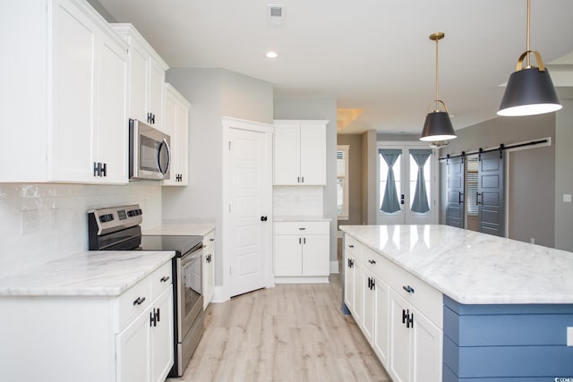 kitchen featuring a barn door, light wood-style flooring, white cabinets, hanging light fixtures, and appliances with stainless steel finishes