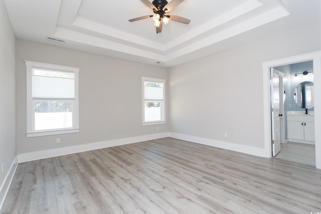 spare room featuring a raised ceiling, visible vents, light wood-style flooring, and baseboards