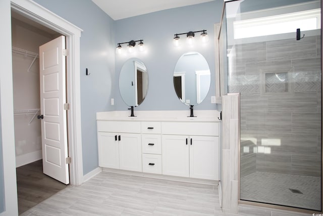 bathroom with double vanity, a shower stall, baseboards, and a sink