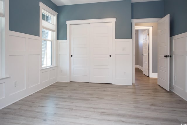 unfurnished bedroom with a decorative wall, a closet, wainscoting, and light wood-style floors