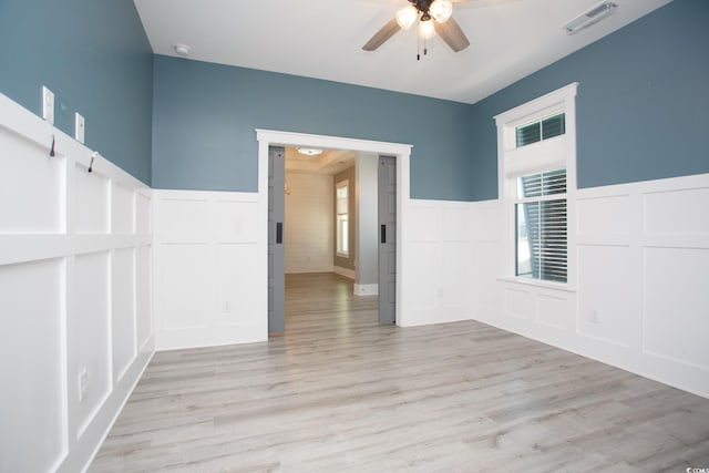 unfurnished room featuring light wood-style floors, visible vents, a decorative wall, and a ceiling fan