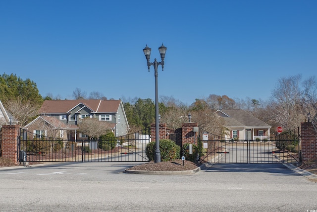 view of road featuring curbs, street lighting, a gated entry, and a residential view