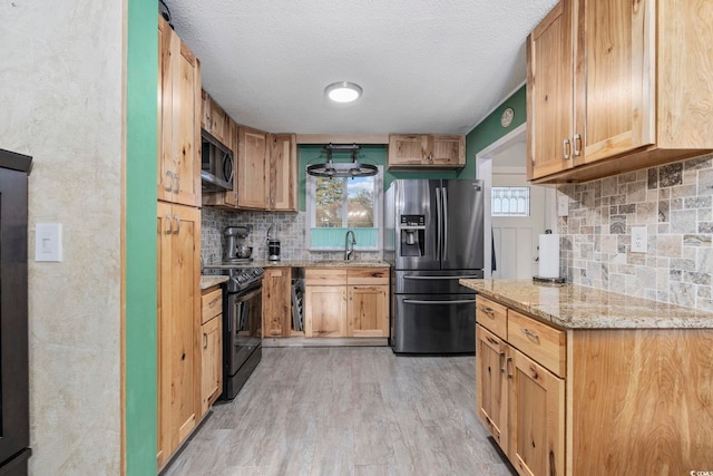 kitchen featuring sink, electric range, light stone counters, stainless steel refrigerator with ice dispenser, and light hardwood / wood-style flooring