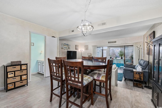 dining space with a textured ceiling, a notable chandelier, and light wood-type flooring