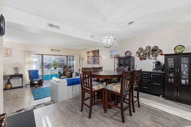 dining area with a chandelier, light hardwood / wood-style floors, and a textured ceiling