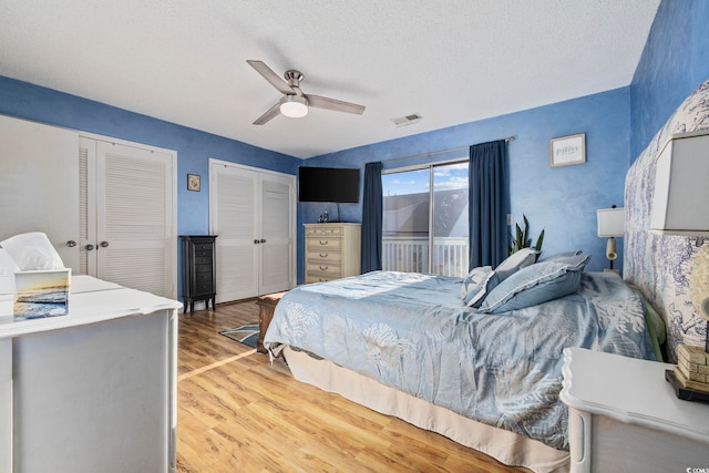 bedroom featuring hardwood / wood-style floors, ceiling fan, two closets, and a textured ceiling