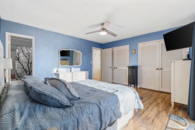 bedroom featuring multiple closets, ceiling fan, a textured ceiling, and light hardwood / wood-style flooring