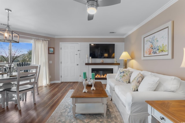 living room featuring ceiling fan with notable chandelier, dark wood-type flooring, and ornamental molding