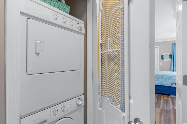 laundry area featuring crown molding, wood-type flooring, and stacked washing maching and dryer