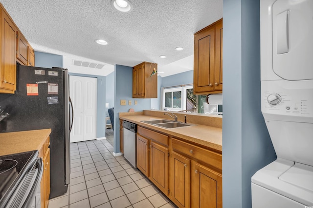 kitchen with appliances with stainless steel finishes, sink, stacked washer and dryer, light tile patterned floors, and a textured ceiling