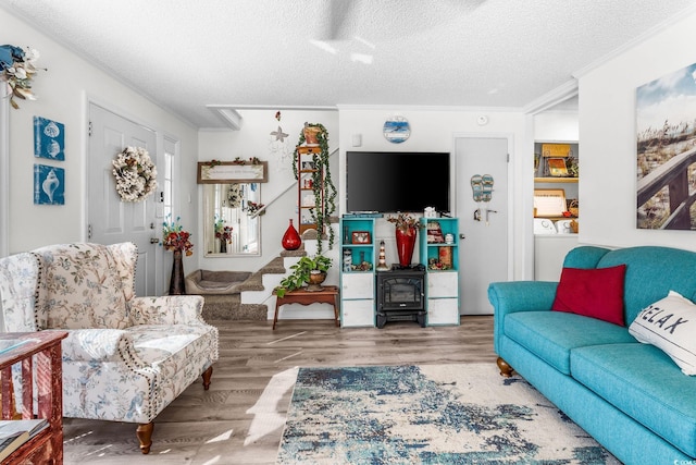 living room with washer / dryer, crown molding, a textured ceiling, a wood stove, and hardwood / wood-style floors