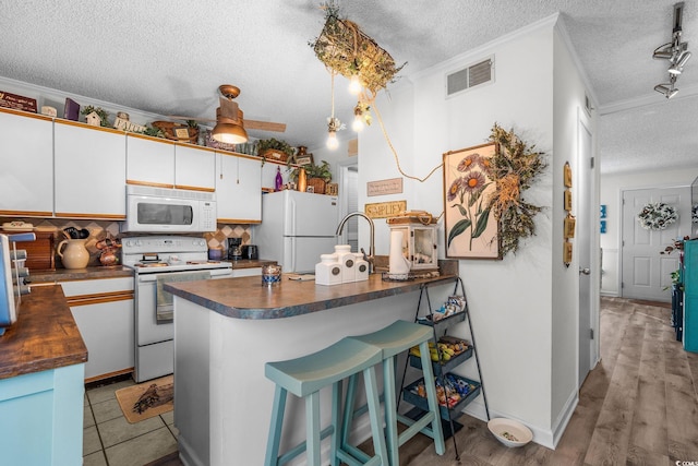 kitchen with a textured ceiling, ornamental molding, a kitchen breakfast bar, white appliances, and white cabinets