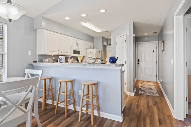 kitchen with dark hardwood / wood-style flooring, white cabinets, white appliances, and kitchen peninsula