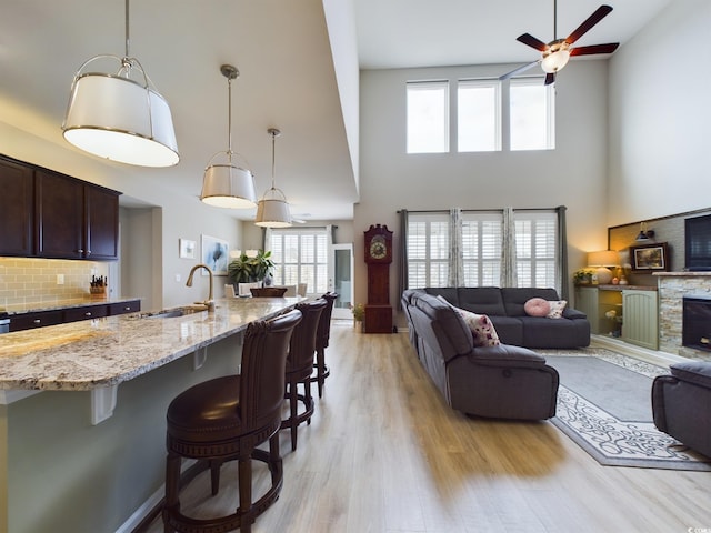 living room with a towering ceiling, light wood-style floors, a fireplace, and a ceiling fan