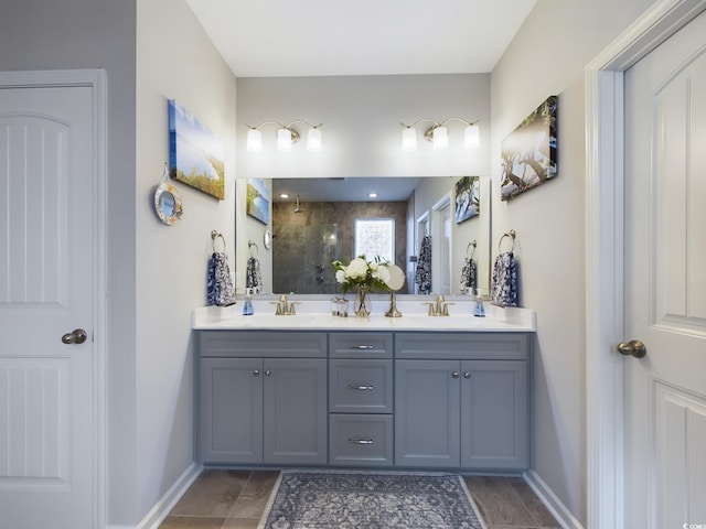 full bathroom with double vanity, baseboards, a tile shower, and a sink