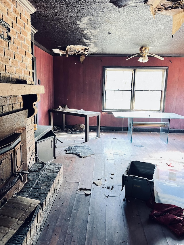 misc room with hardwood / wood-style floors, wood walls, ceiling fan, a brick fireplace, and a textured ceiling