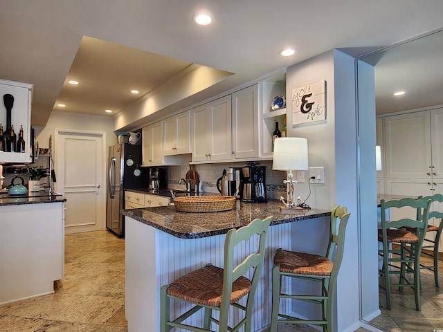 kitchen featuring stainless steel refrigerator, a kitchen breakfast bar, kitchen peninsula, white cabinets, and backsplash