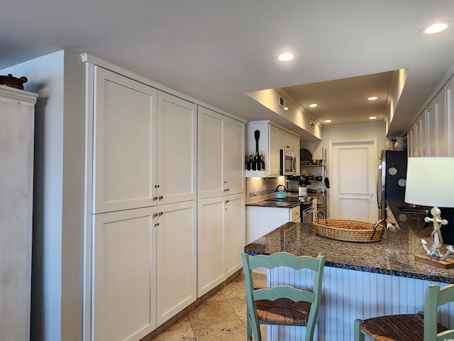 kitchen featuring appliances with stainless steel finishes, dark stone countertops, white cabinets, a kitchen bar, and kitchen peninsula