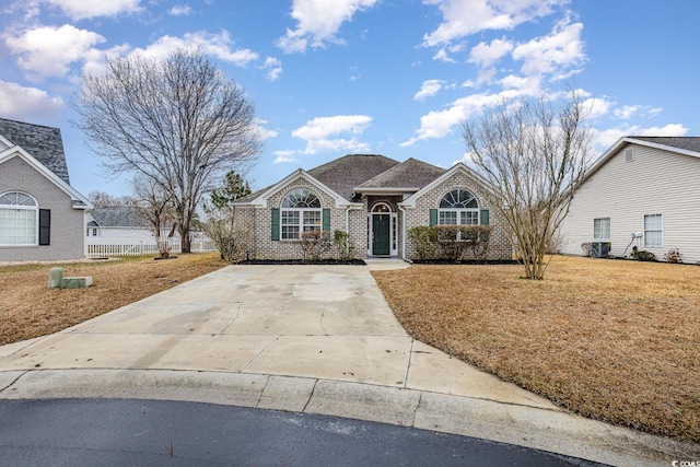 view of front of property with driveway, brick siding, a front lawn, and fence