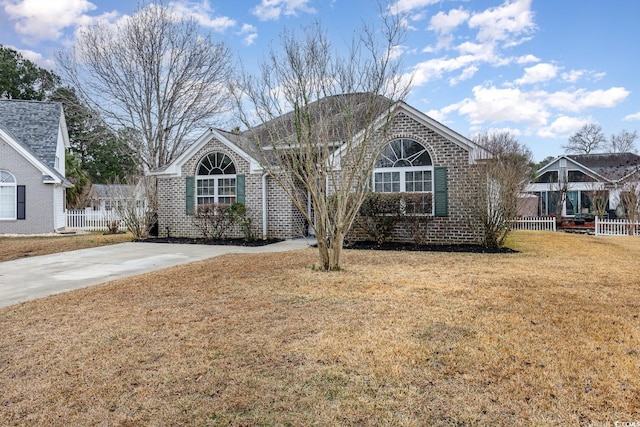 ranch-style house featuring a front yard, brick siding, fence, and driveway