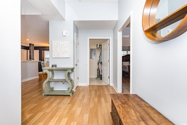 corridor with light wood-style flooring, baseboards, and a textured ceiling