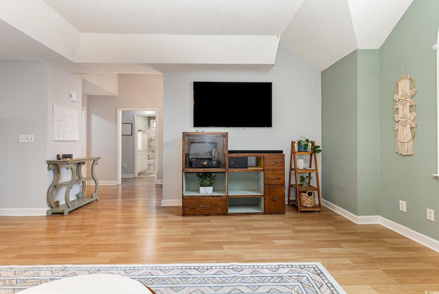 living room featuring lofted ceiling, baseboards, a textured ceiling, and light wood finished floors