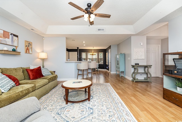 living area featuring a tray ceiling, visible vents, baseboards, and wood finished floors