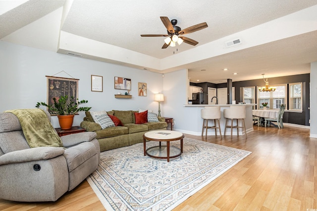 living area featuring baseboards, visible vents, a textured ceiling, light wood-type flooring, and ceiling fan with notable chandelier