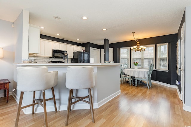 kitchen with a peninsula, black appliances, a kitchen bar, and light wood-style floors