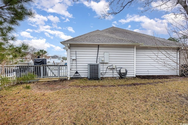 view of side of home featuring central AC unit, a lawn, and roof with shingles