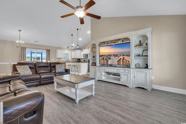 living area with ceiling fan with notable chandelier, high vaulted ceiling, light wood-style flooring, and baseboards