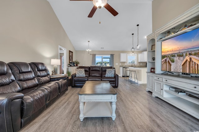 living room with light wood-type flooring, high vaulted ceiling, and ceiling fan with notable chandelier