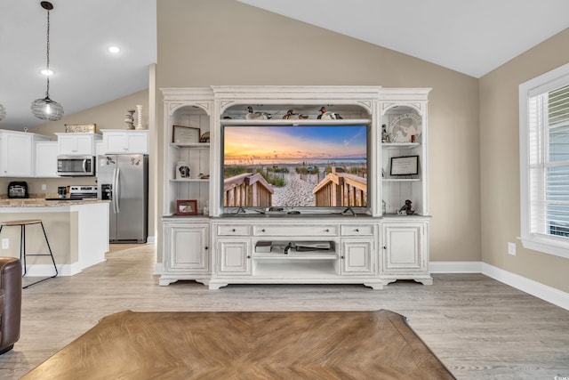 interior space featuring baseboards, light wood finished floors, lofted ceiling, stainless steel appliances, and hanging light fixtures