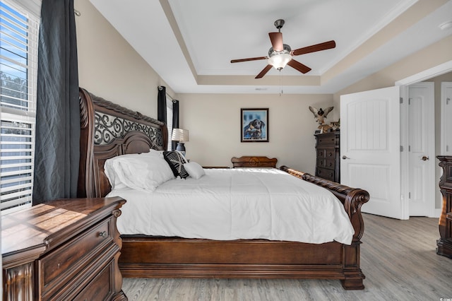 bedroom with a tray ceiling, light wood-style flooring, a ceiling fan, and ornamental molding