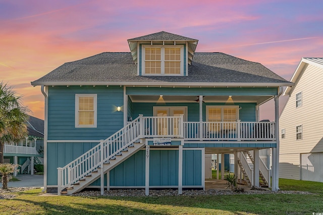 back house at dusk featuring ceiling fan, a yard, and covered porch