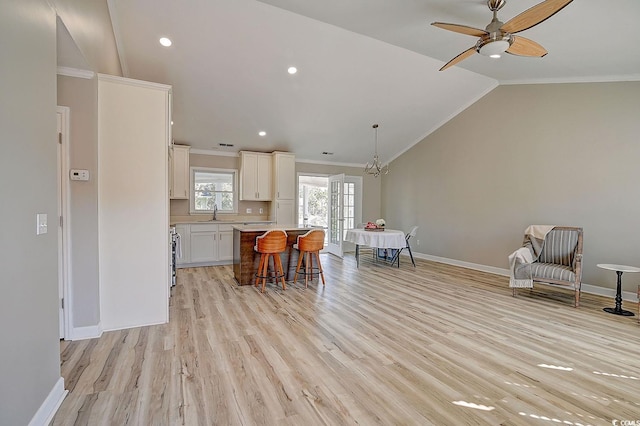 kitchen with a kitchen island, lofted ceiling, a breakfast bar area, white cabinets, and ornamental molding