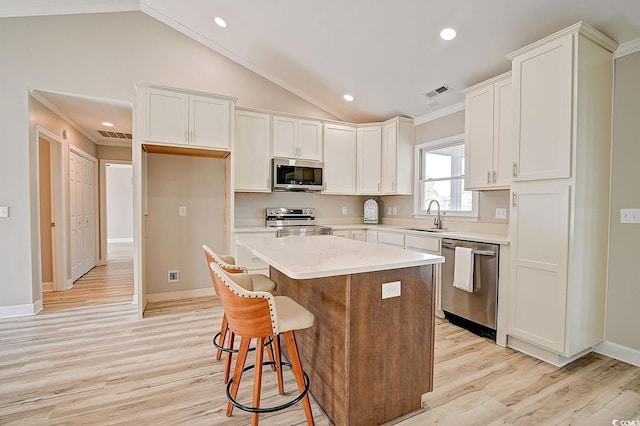 kitchen with sink, white cabinetry, vaulted ceiling, a kitchen island, and stainless steel appliances